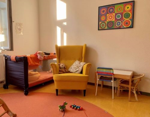 Sessel, Kinderbett und Spielsachen im Eltern-Kind-Zimmer